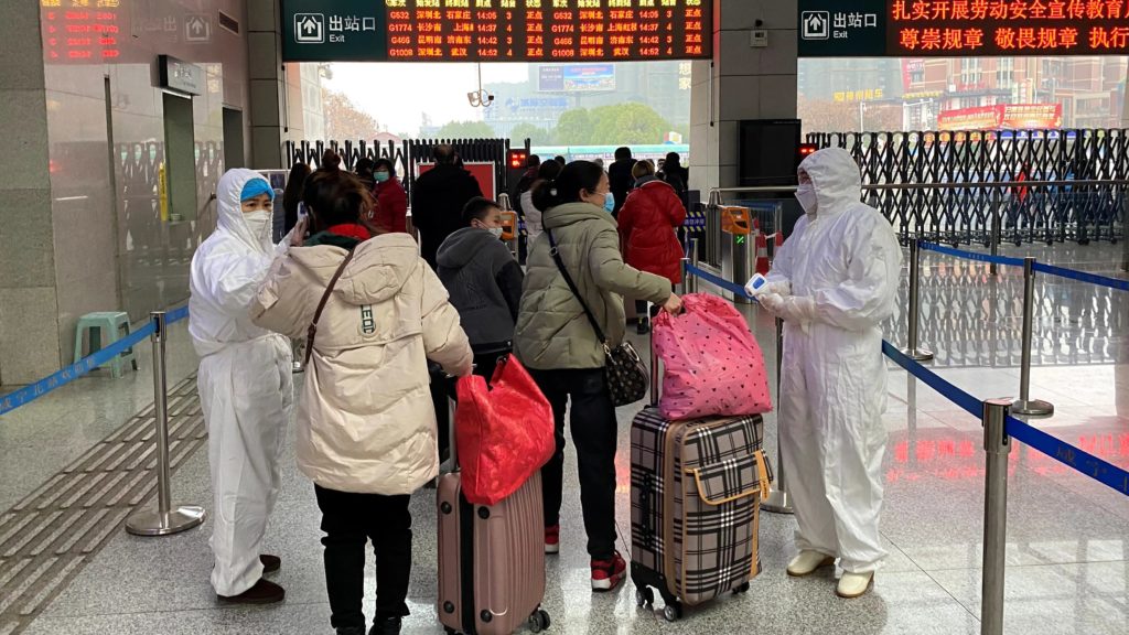 Operatori con tute protettive controllano la temperatura dei passeggeri arrivati alla stazione di Xianning, una città confinante con Wuhan (crediti: Reuters)