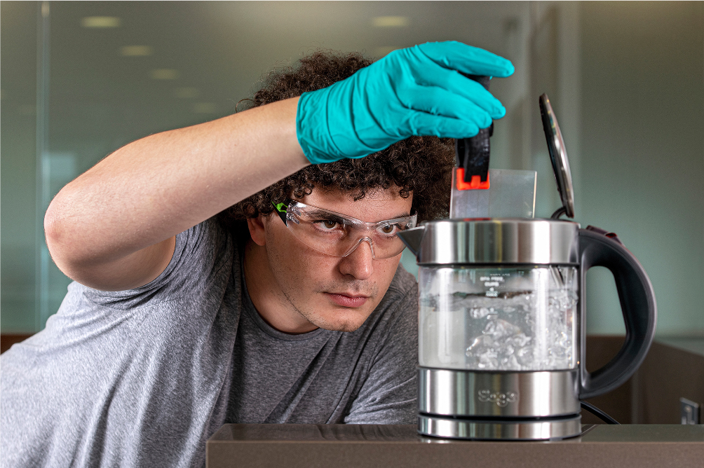 Microsoft Project Silica researcher Youssef Assaf drops a square of silica glass in a kettle of boiling water to demonstrate its durability. The team has baked, boiled, microwaved, demagnetized and scoured similar pieces of glass with steel wool — with no