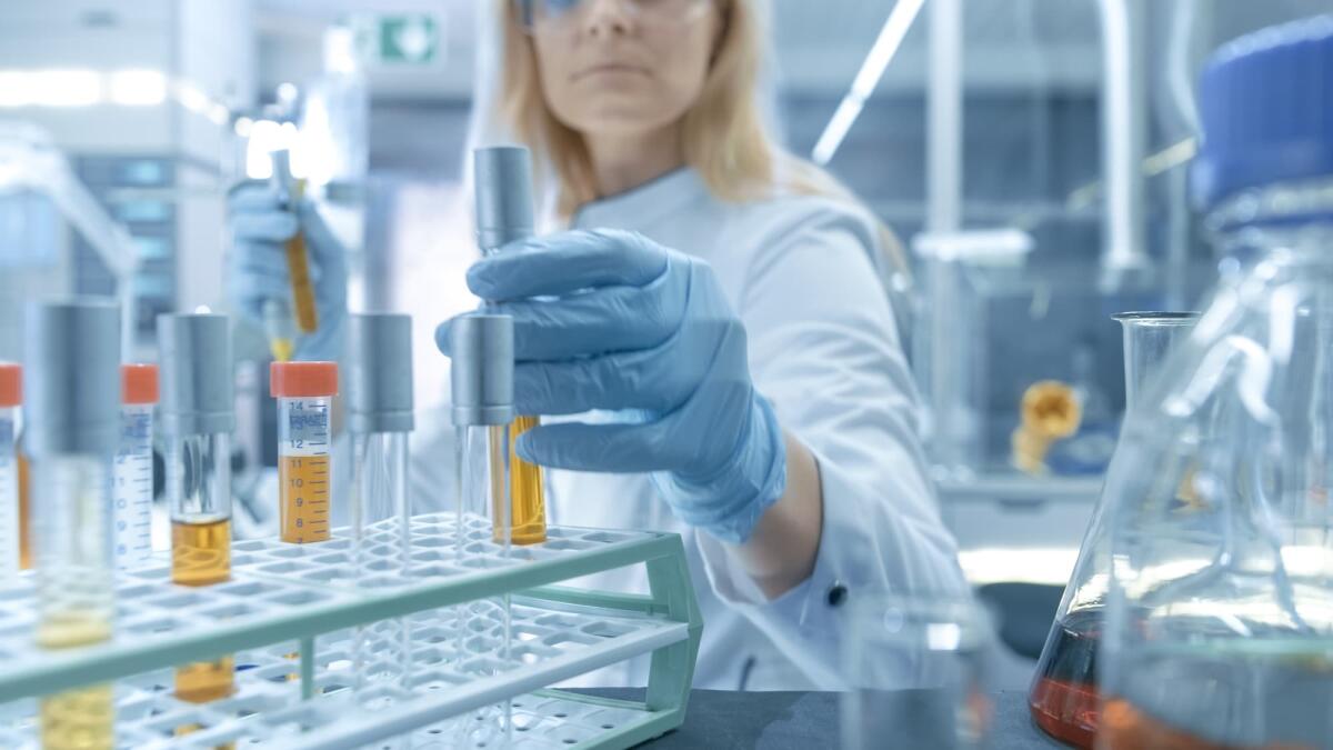 L'importanza di manipolare un virus in laboratorio per la ricerca scientifica - Medical Virology Research Scientist Works in a Hazmat Suit with Mask, Inspects Test Tube with Isolated Virus String from Refrigerator Box. She Works in a Sterile High Tech Laboratory/ Research Facility.