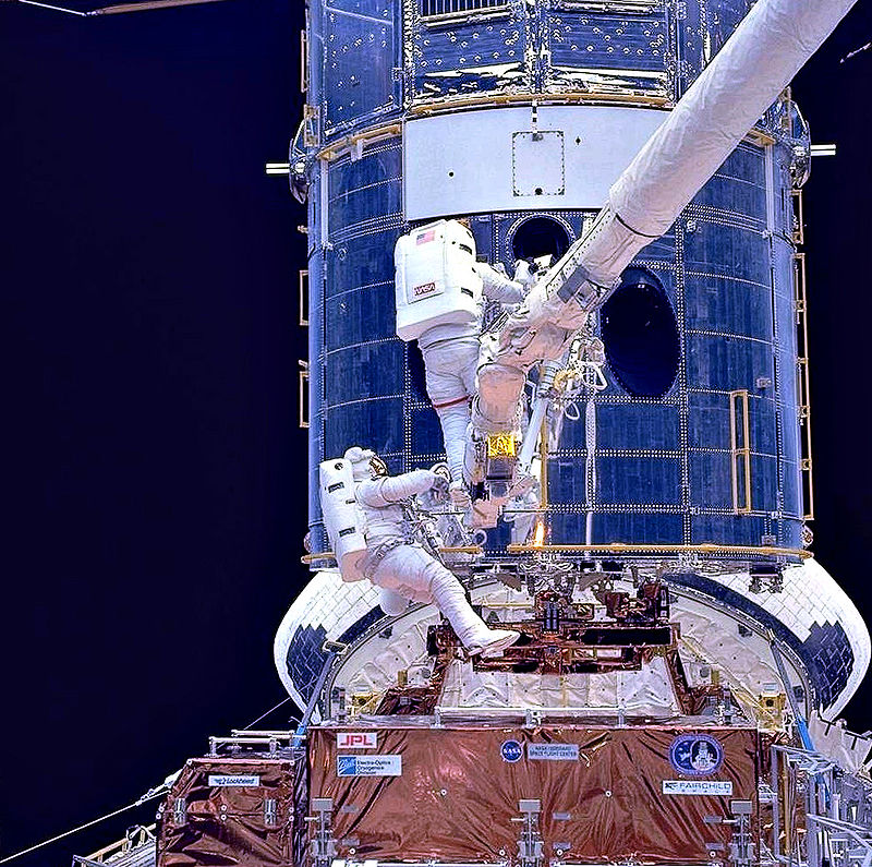 Gli astronauti Musgrave e Hoffman installano le ottiche correttive durante la SM1 (Wikipedia)