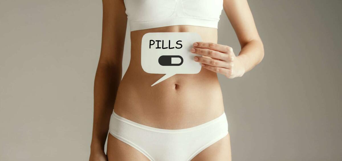 Una videocapsula "intelligente" per esaminare l'intestino tenue - Woman health. Female model holding card with word PILLS near stomach. Young adult girl with paper for sign or symbol isolated on gray studio background. Cut out part of body. Medical problem and solution.