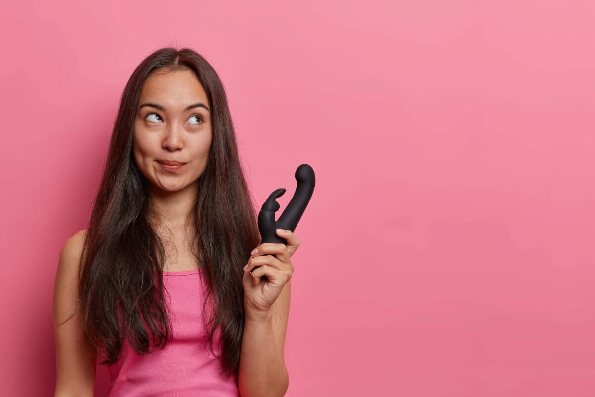 La tecnologia dei sex toys: l'ingegneria al servizio del piacere - Horizontal shot of thoughtful Asian woman holds rabbit shaped vibrator, uses erotic toy for pleasuring, buys vibrating sex toys for adults, gets relaxation and pleasure. Vaginal exercise machine