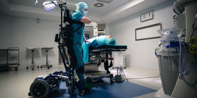 In foto Marco Dolfin in posizione eretta grazie alla nuova carrozzina realizzata appositamente per lui che esegue un'operazione ortopedica, sono visibili le bretelle che rendono stabile il chirurgo durante l'operazione - Credits: scatto di Francesco A. Ar