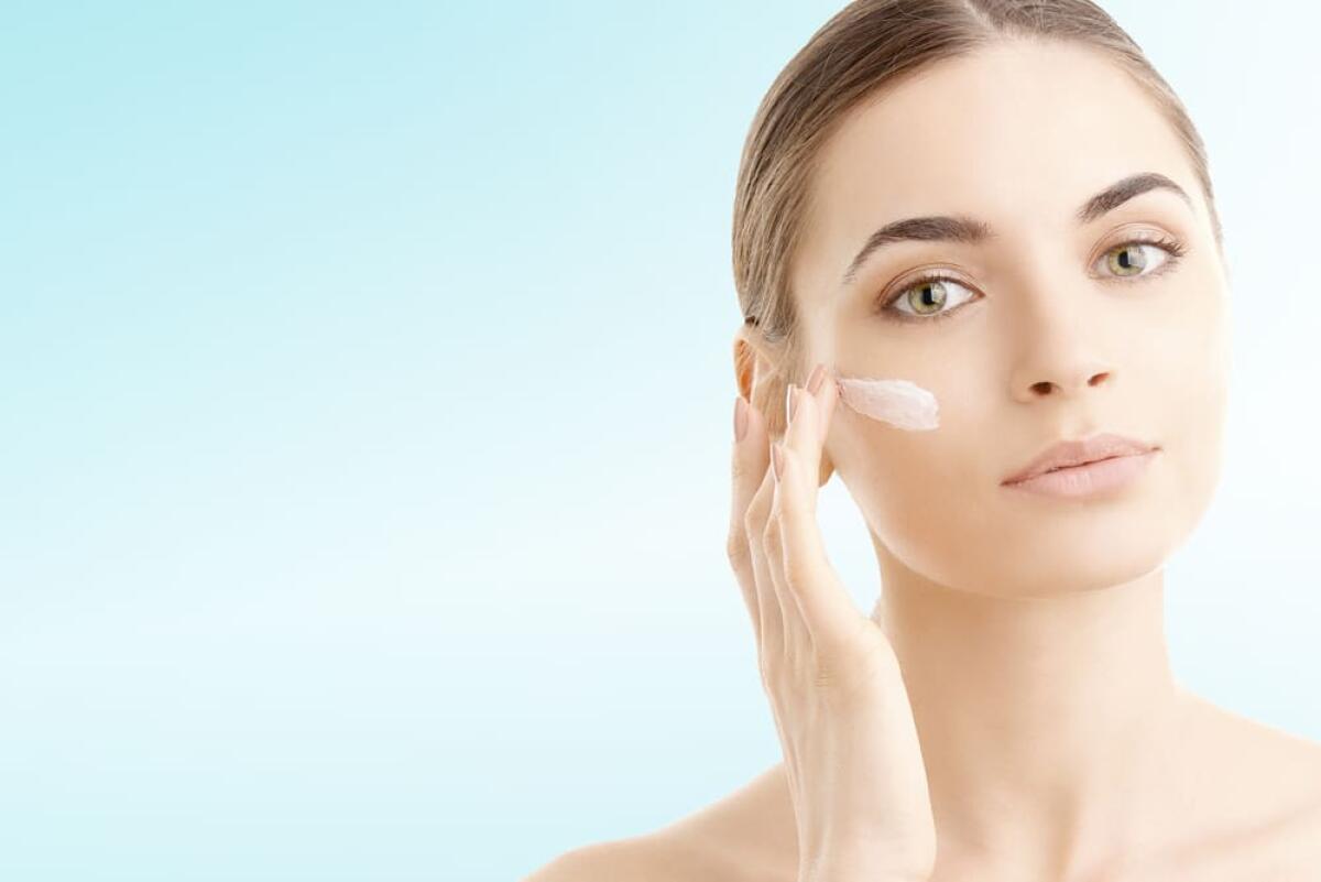 I 5 prodotti anti age immancabili in una trousse - Studio shot of a beautiful young woman applying moisturizer onto her face against a blue background with copy space.