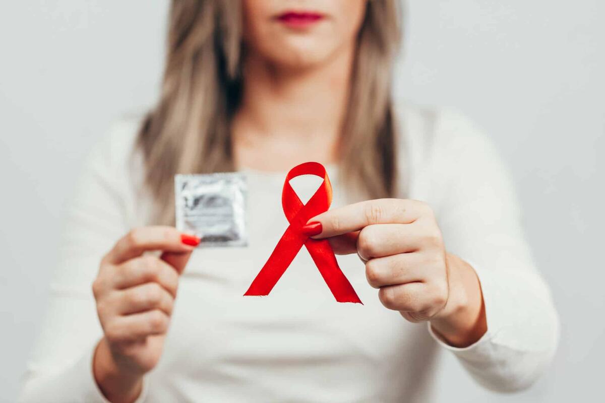 AIDS: cos'è, sintomi, protezione, differenze con l'HIV - Woman holding condom and red ribbon for HIV illness awareness, 1 December World AIDS Day concept.