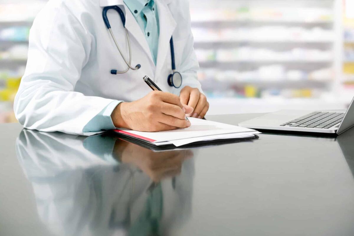 Google Lens: leggerà l'indecifrabile calligrafia dei medici - Male pharmacist sitting at table and writing on a document report in pharmacy office. Medical healthcare staff and pharmaceutical service.