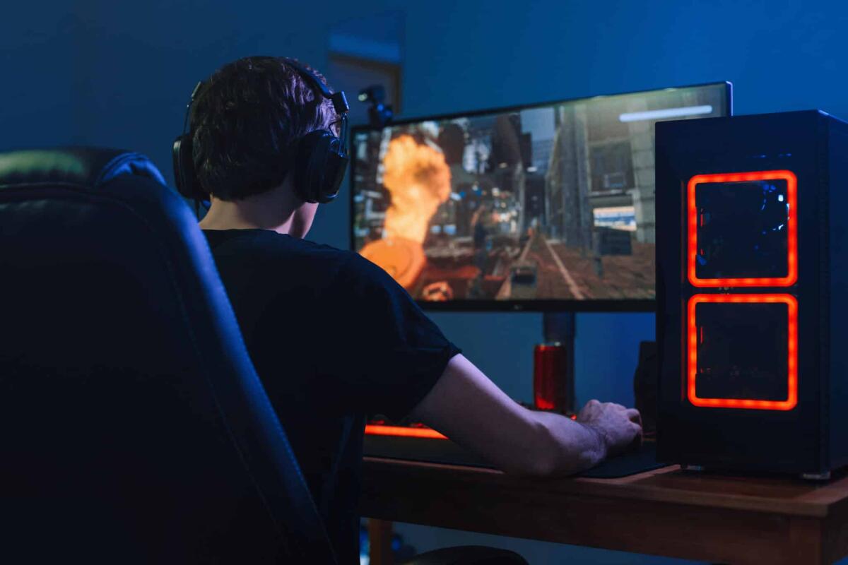 Durante le feste si gioca di più - Young professional gamer playing tournaments online video games on computer with headphones in his room, red and blue neon color. Cybersport concept. Back view