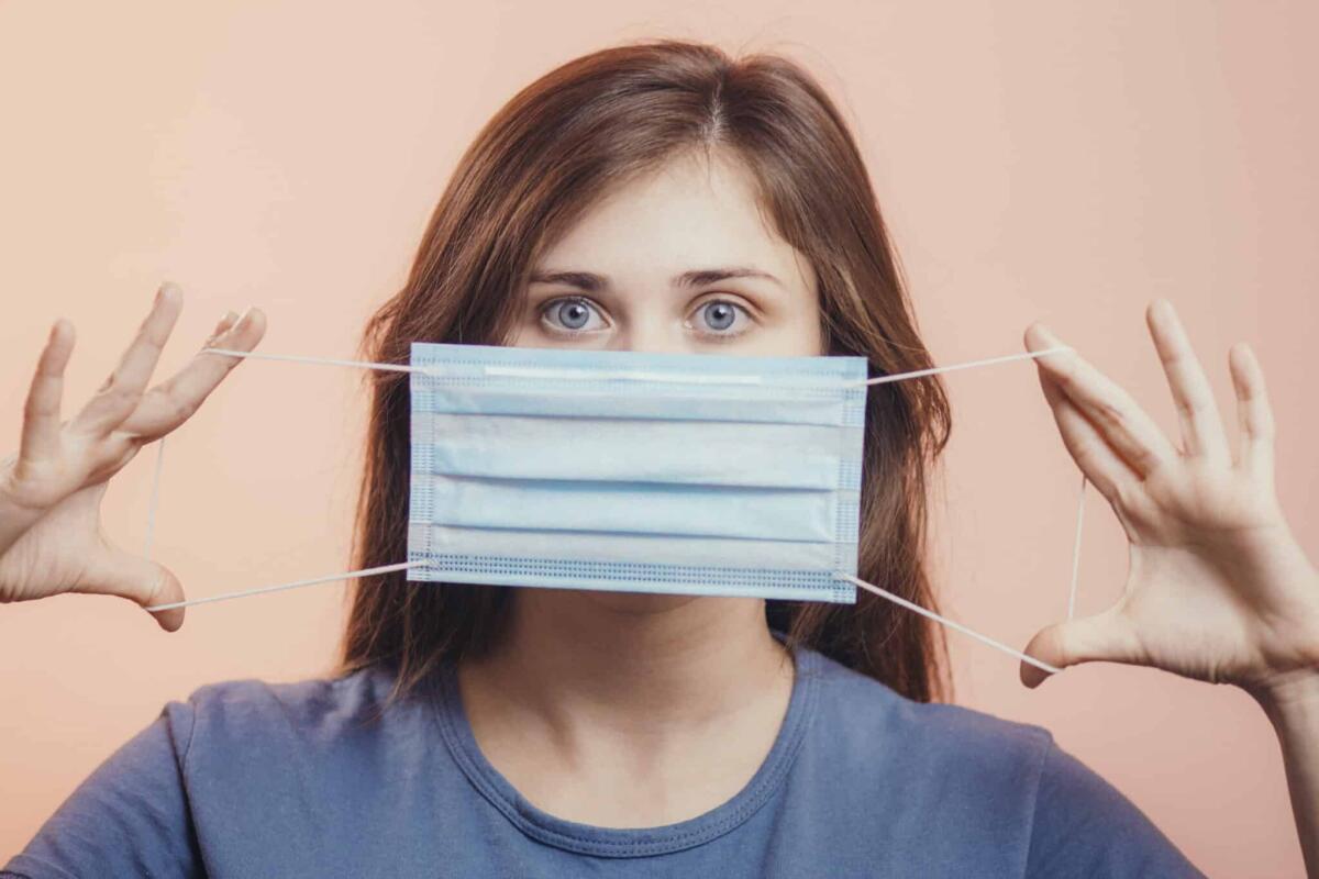 Le prime mascherine che fermarono la peste in Manciuria - Portrait of young woman showing opened medical flu mask covering face on colored studio background, girl looking with scared eyes, quarantine measures