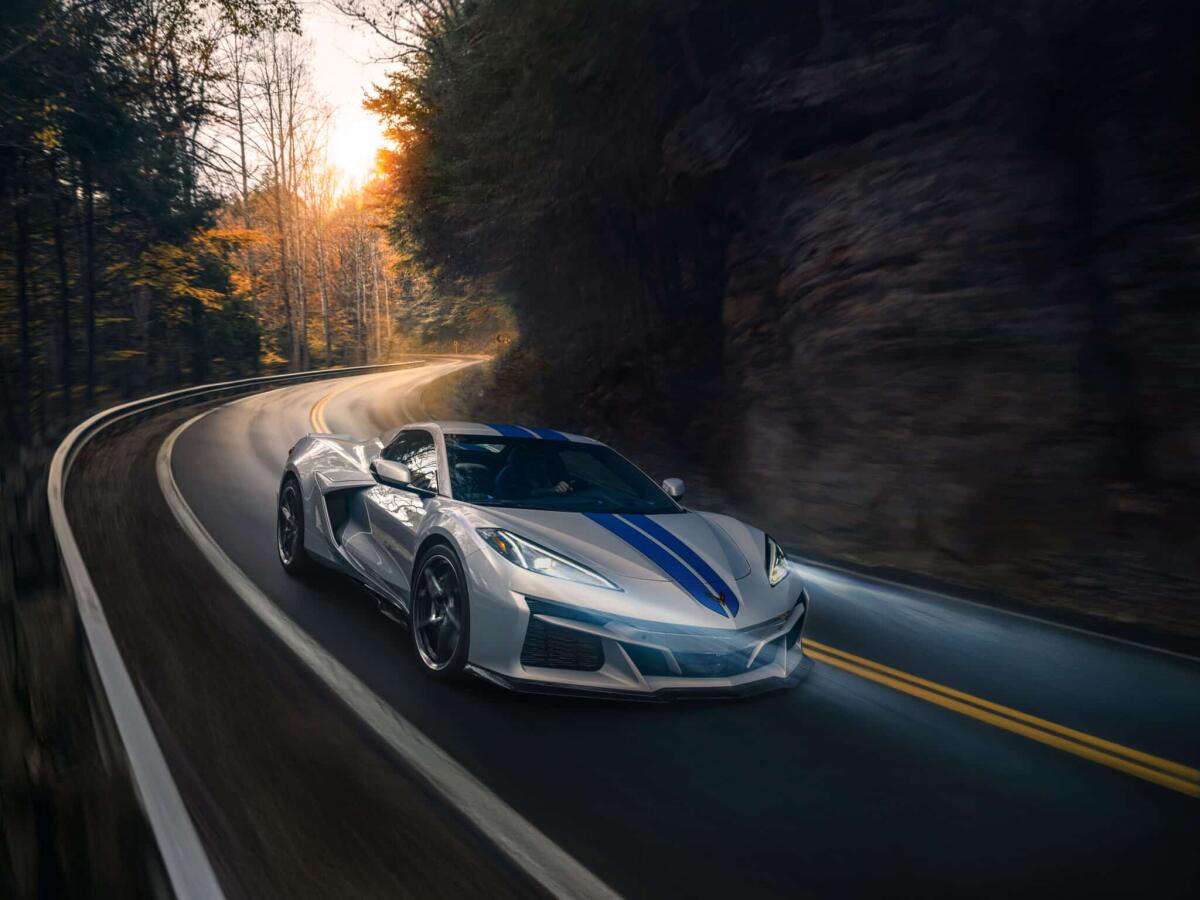 Chevrolet Corvette C8 E-Ray AWD: ecco la prima Corvette ibrida e con trazione integrale - Passenger side front 3/4 view of 2024 Chevrolet Corvette E-Ray 3LZ convertible in Silver Flare with Electric Blue stripe package driving on a curved mountain road. Pre-production model shown. Actual production model may vary. Model year 2024 Corvette