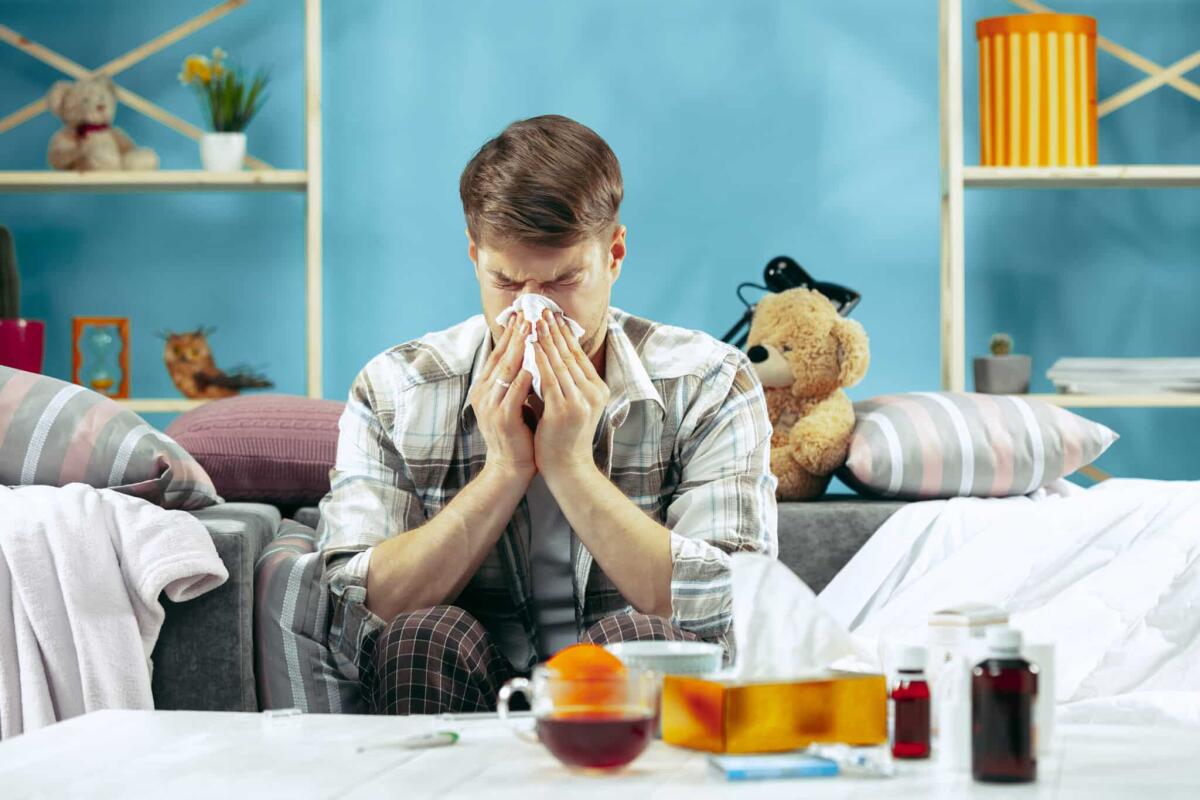 Il raffreddore per gli uomini non è più pesante, lo conferma uno studio - Bearded sick man with flue sitting on sofa at home and blowing his nose. The winter, illness, influenza, pain concept. Relaxation at Home. Healthcare Concepts.