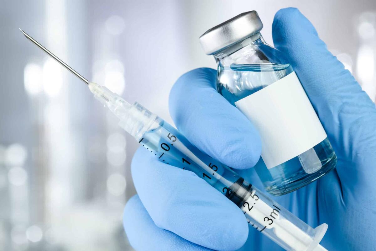 Vaccini antitumorali: scopo e funzione - Healthcare concept with a hand in blue medical gloves holding a vaccine vial with blue liquid and black white label