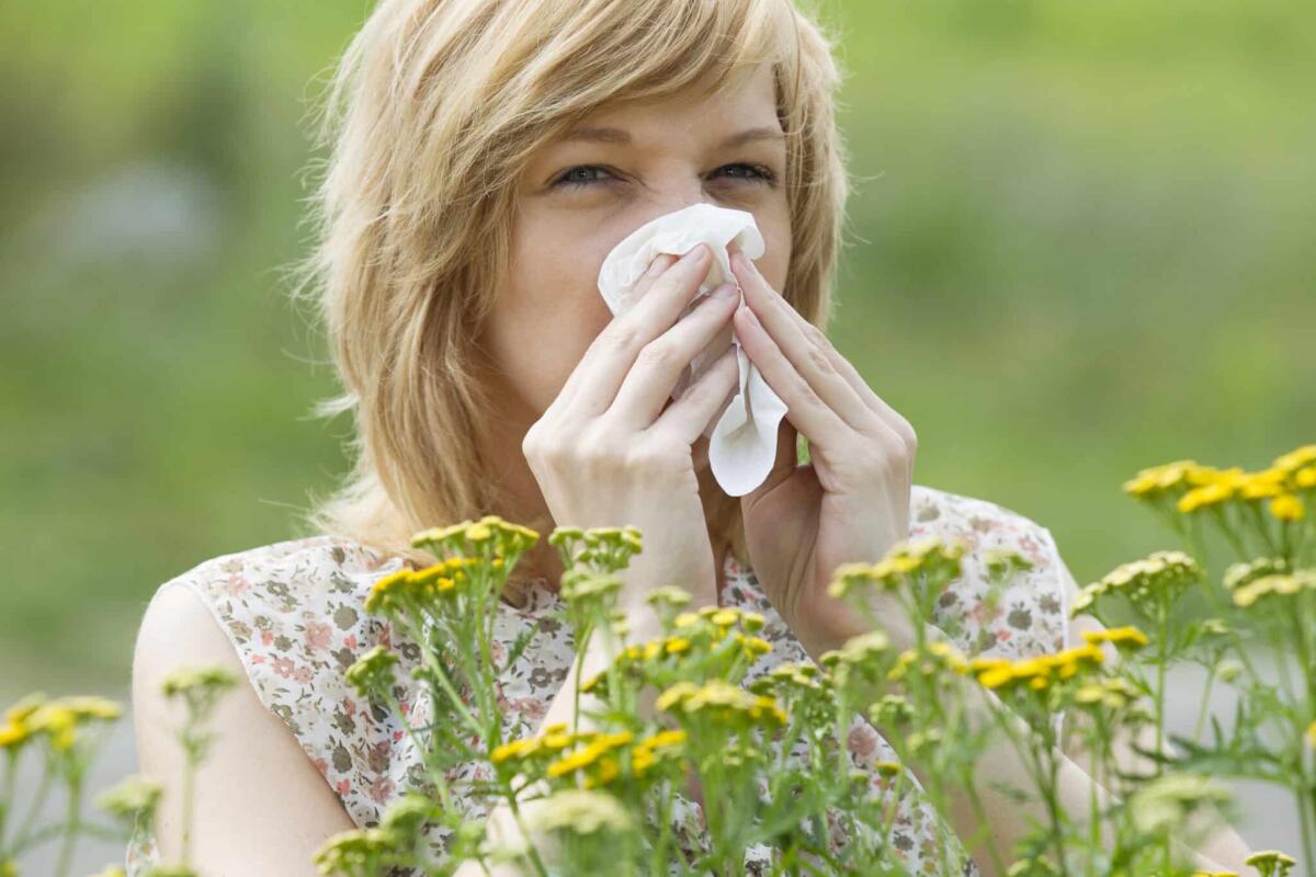 Allergia al polline: sintomi, diagnosi e cure - Young woman blowing nose into tissue in front of flowers