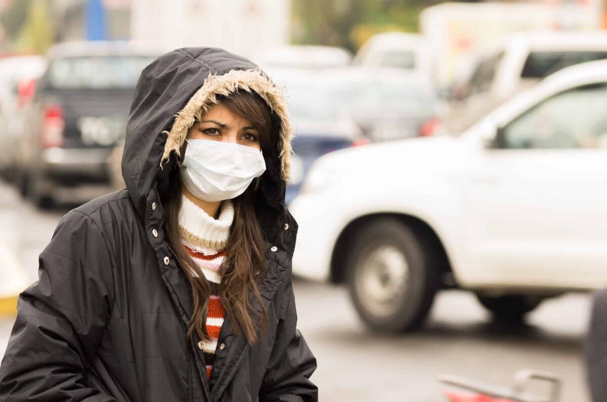 L'inquinamento atmosferico aumenta il rischio di demenza - portrait of young girl walking wearing jacket and a mask in the city street concept of  pollution