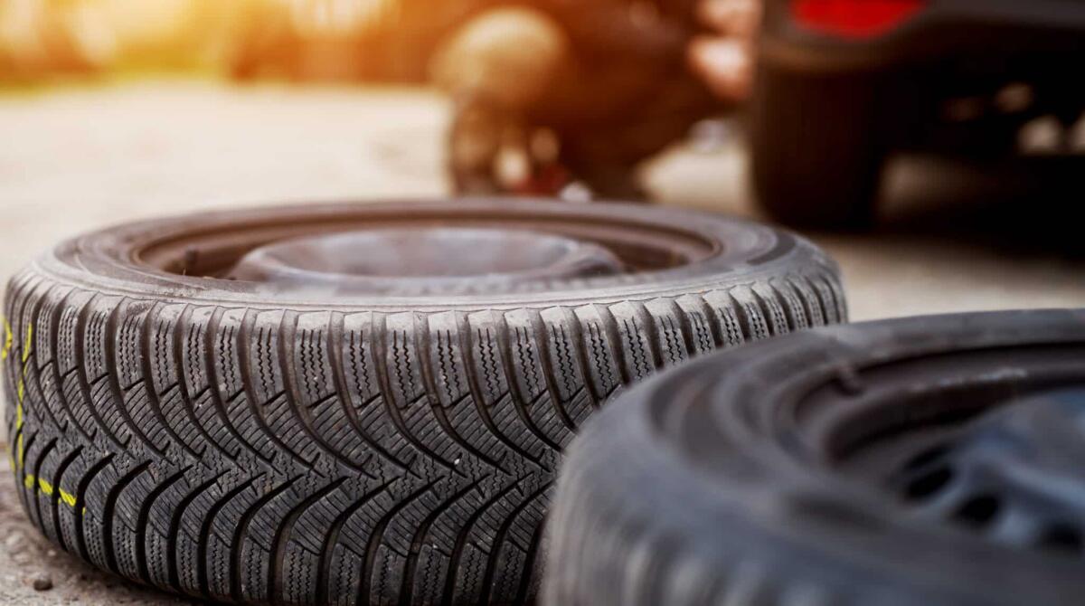 L'importanza di scegliere i giusti pneumatici - New tire laying on the pavement near the mechanic ready to replace the one on a car.