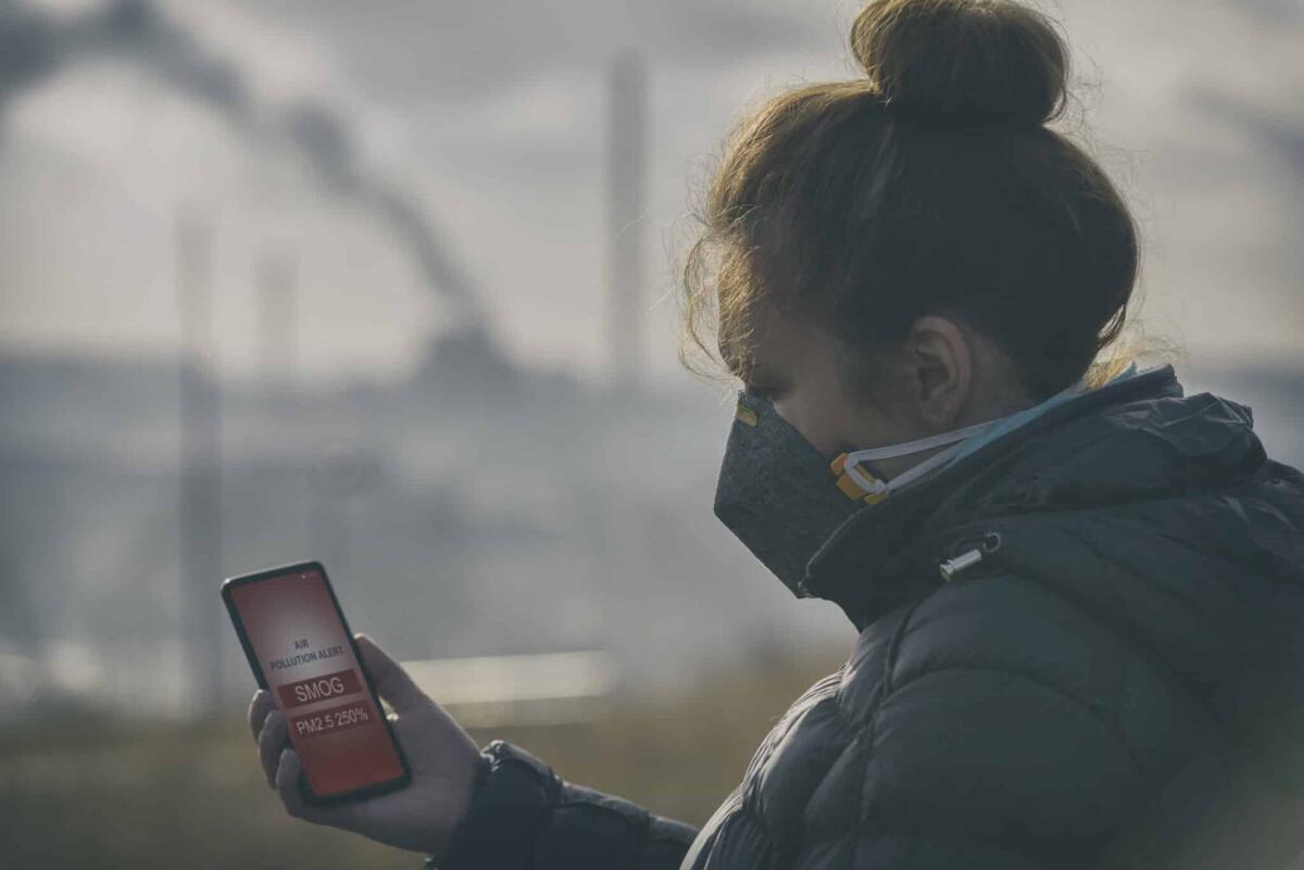 Uno studio dimostra come il sole e l'inquinamento abbiano influenzato sul Covid in Lombardia - Woman wearing a real anti-pollution, anti-smog and viruses face mask and checking current air pollution with smart phone app