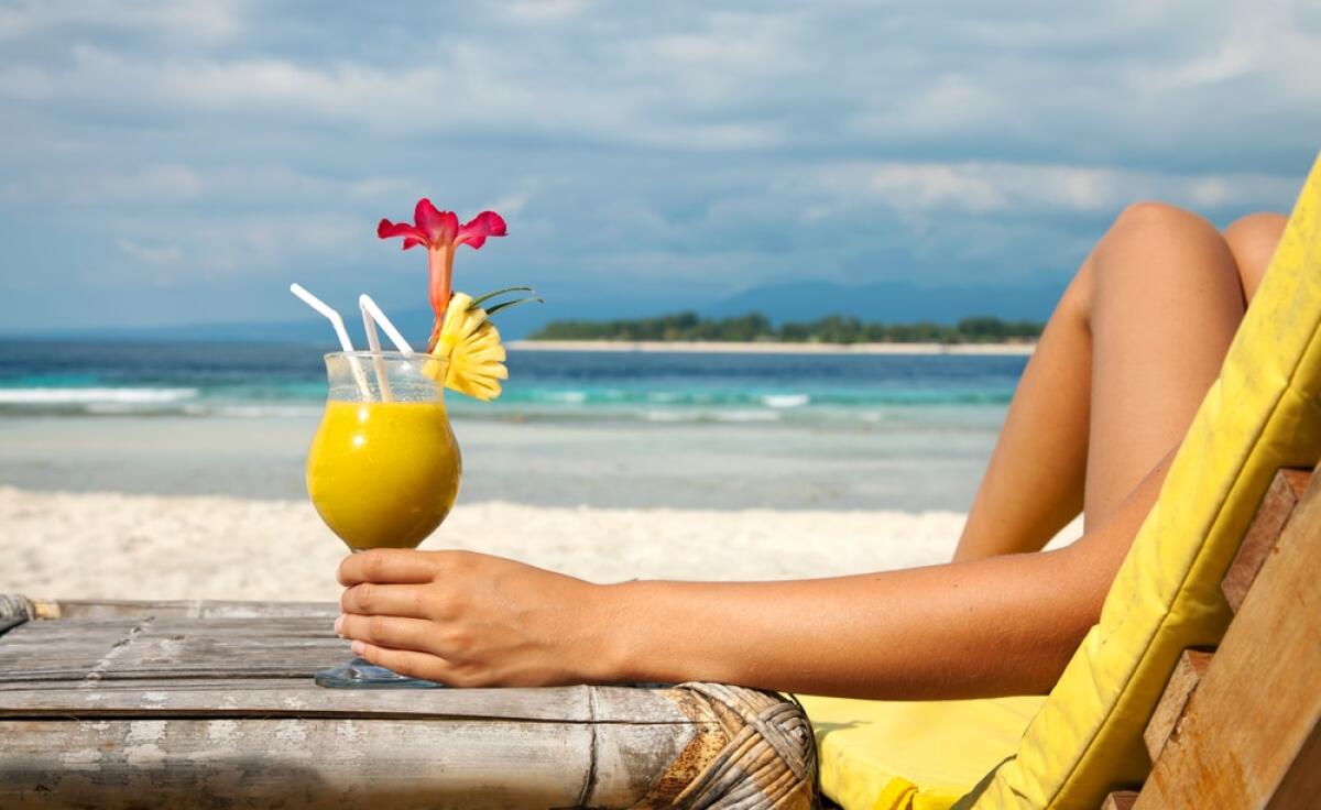 Bonus Vacanze 2023: come richiederlo e agevolazioni previste - Woman holding a fruit cocktail on a tropical beach
