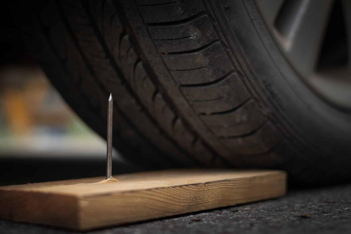 Pneumatici runflat: cosa sono e quali vantaggi che offrono? - Close up a metal nail on board wood nearly to puncture into wheel tire