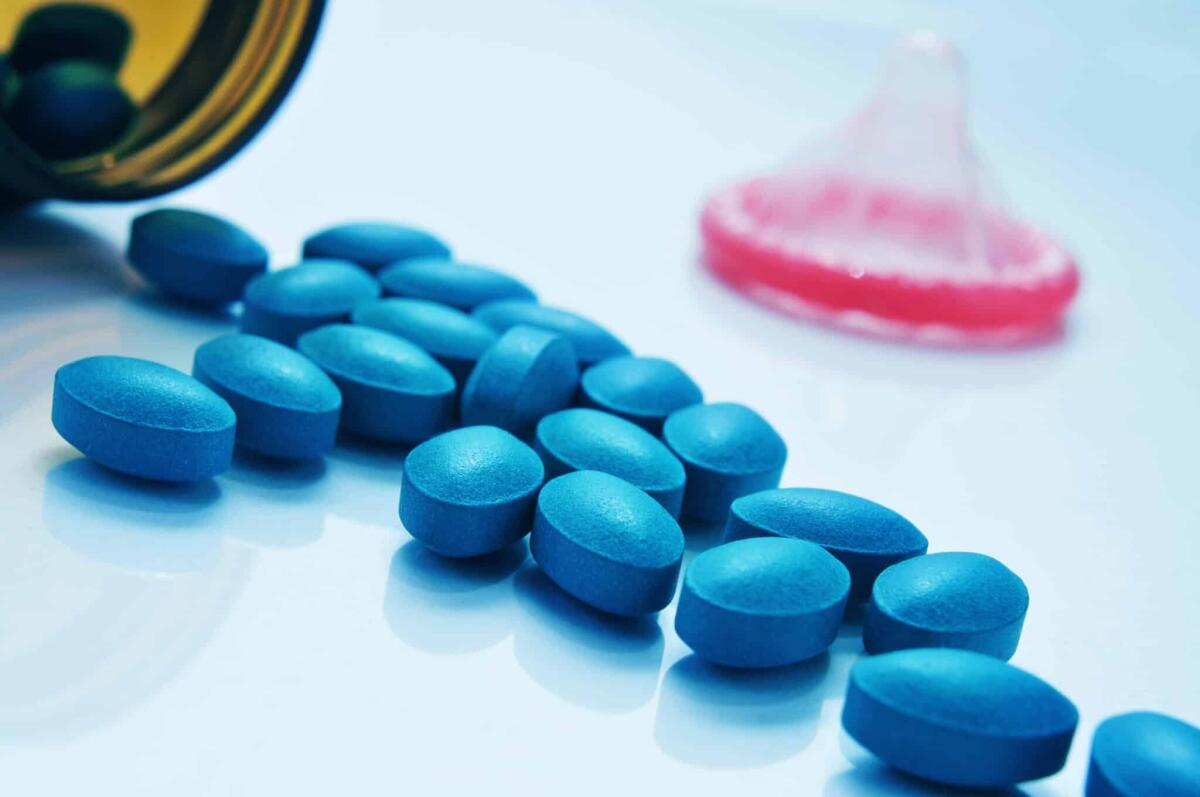 Acquisto Viagra online: è possibile in Italia senza ricetta? - a pile of blue pills coming out of a bottle and a condom in the background