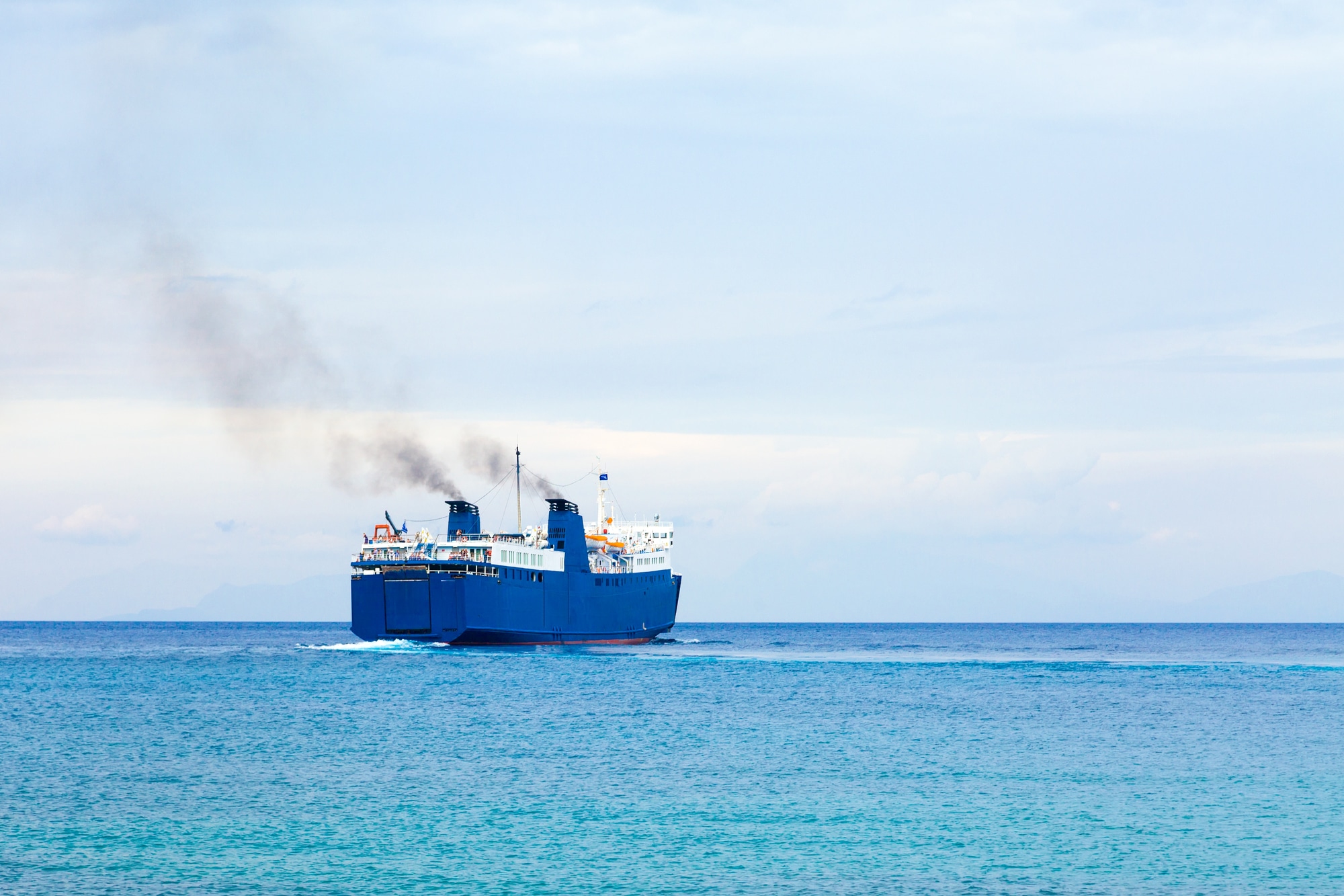 Big cargo ship and ferry boat in the turquoise waters of the mediterranean sea.