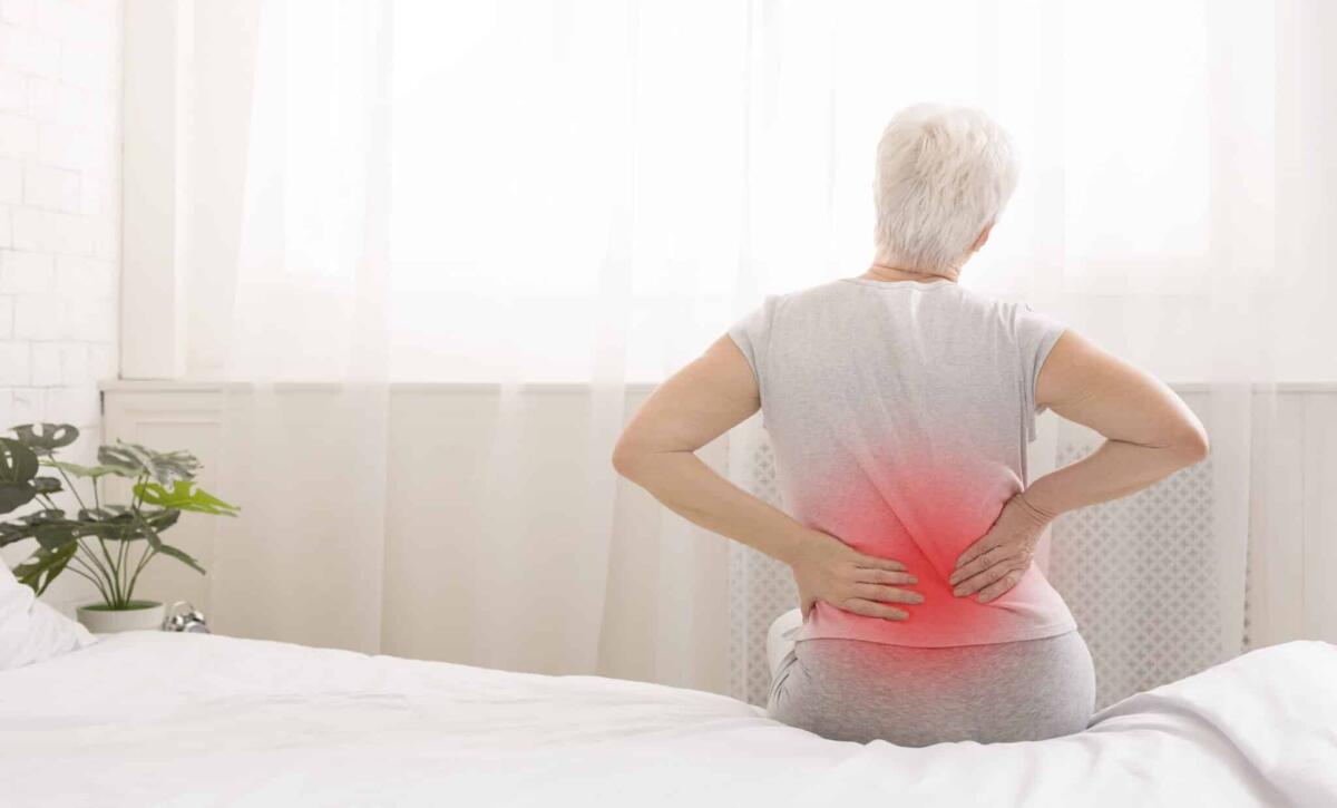 La donna che non sente dolore a causa di una mutazione genetica - Senior woman suffering from backache in morning sitting on bed, red sore zone, panorama with free space
