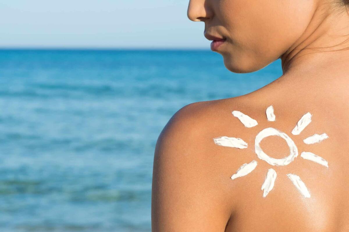 Consigli per proteggere la pelle dal sole - Woman With Suntan Lotion At The Beach In Form Of The Sun