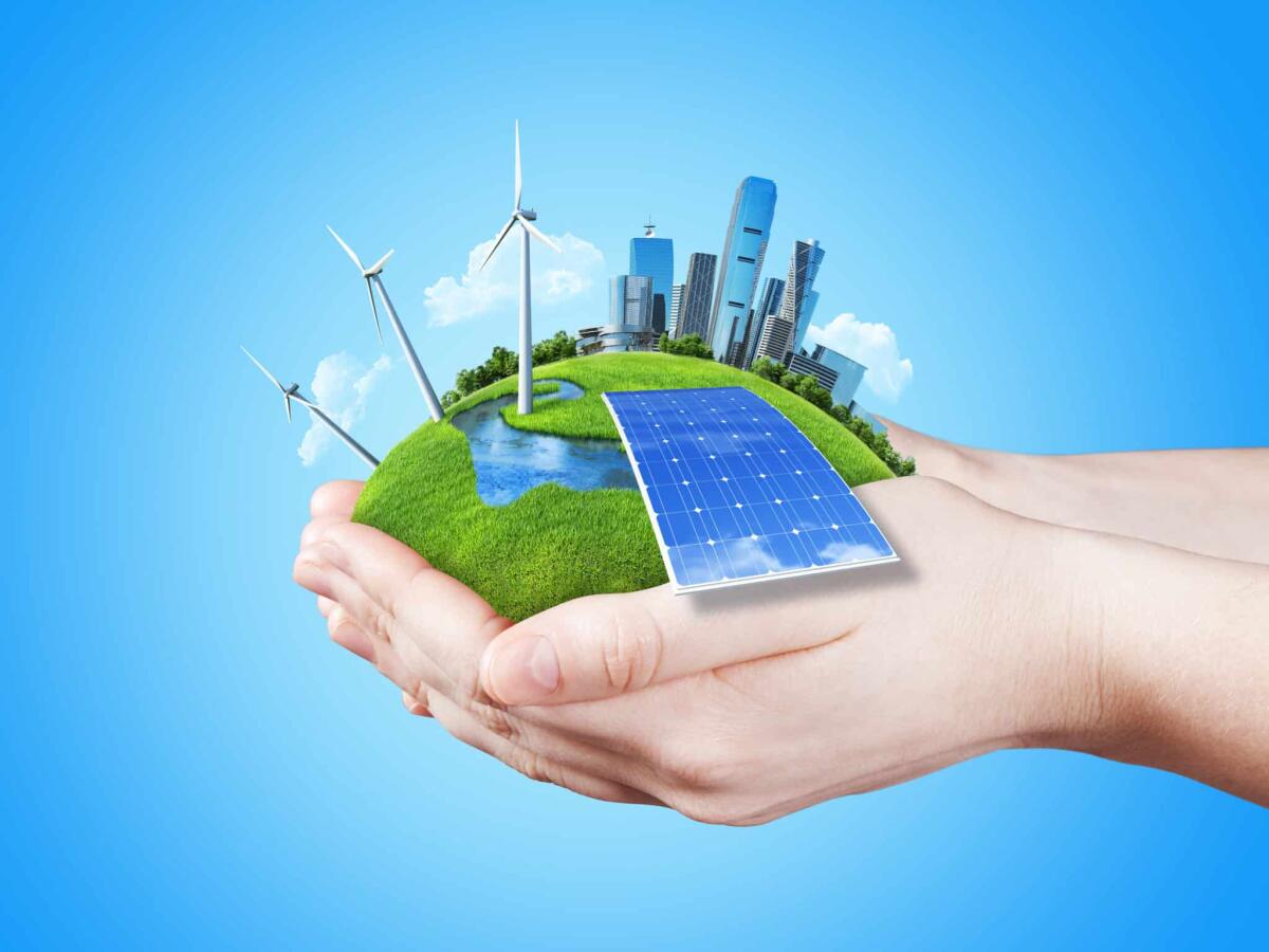 Thermotoga neapolitana: il batterio che produce energia dai rifiuti - Hands holding clear green meadow with sun battery block, wind mill turbines and city skyscrapers. Concept for ecology, growing business, freshness, freedom and other lifestyle issues. Green fields collection.