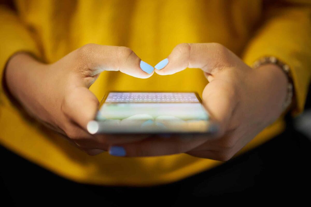 No IT-Alert: coloro che contrastano il sistema di allarme pubblico - Young woman using cell phone to send text message on social network at night. Closeup of hands with computer laptop in background