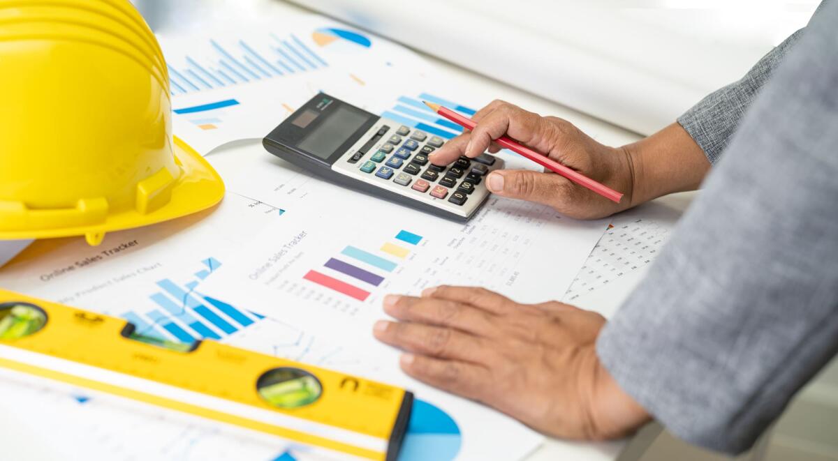 Computo metrico, tutti gli aspetti da sapere - Asian engineer with architectural house plan project blueprint, graph and yellow helmet and engineering construction tools.