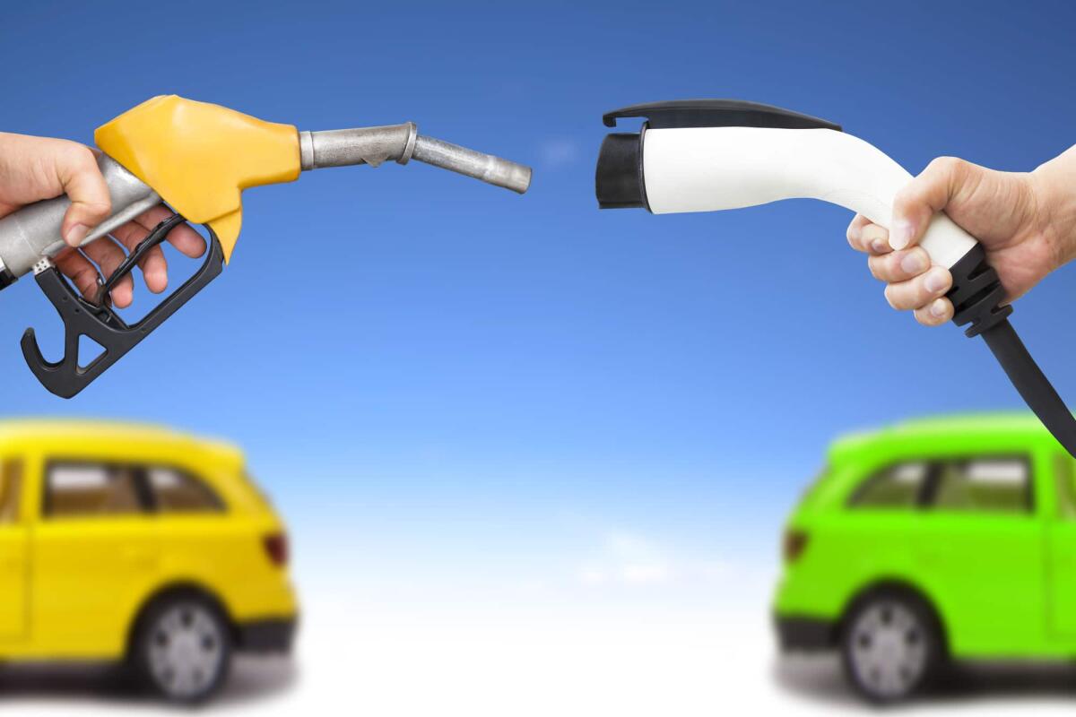 Auto ibride, come orientarsi in fase di scelta - electric car and gasoline car concept. hand holding gas pump and power connector for refuel