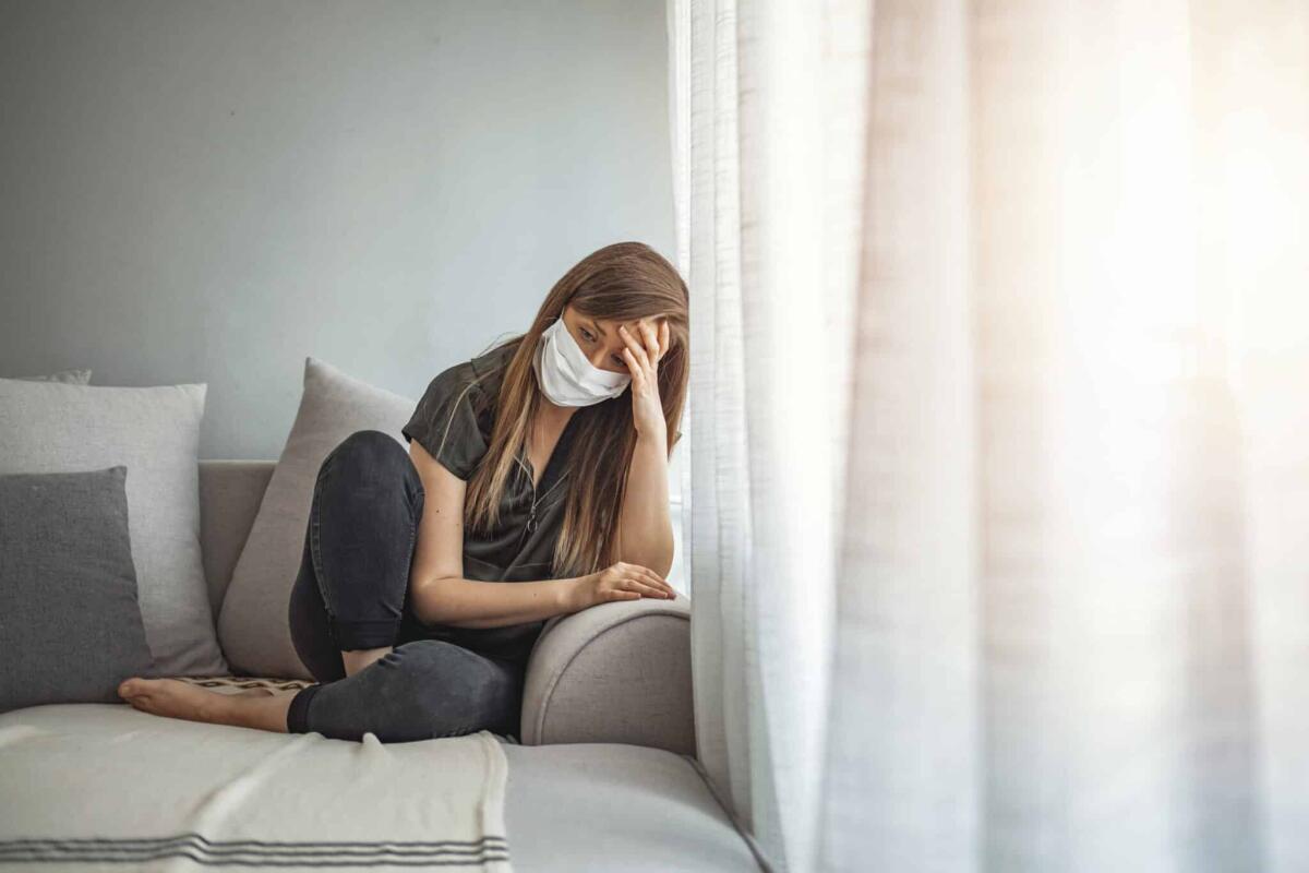 Uno studio identifica delle anomalie multiorgano in pazienti post COVID-19 - Sad lonely girl isolated stay at home in protective sterile medical mask on face looking at window, bored woman because of Chinese pandemic coronavirus virus covid-19. Quarantine, prevent infection