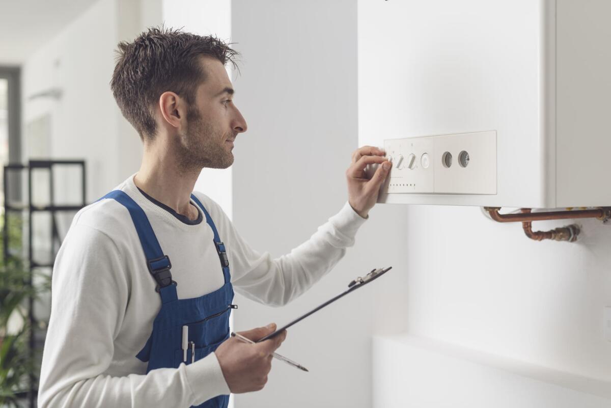 Quanto si risparmia con una caldaia a condensazione? - Professional plumber checking a boiler control panel, he is adjusting a knob