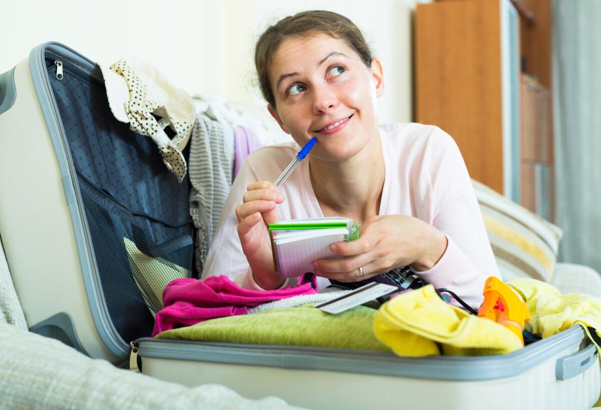 Partire per le vacanze, le cose da ricordarsi di fare a casa - Young brunette planning vacation with notebook and notes on sofa