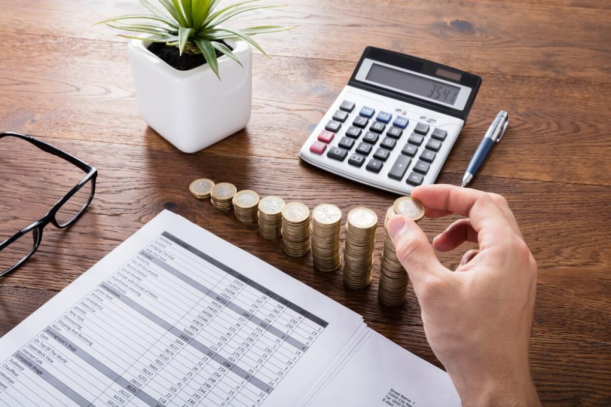 Stangata d'autunno per gli italiani: aumenti su bollette, alimentari, mutui e benzina - Person Stacking Coins With Calculator On Wooden Desk. Investment And Insurance Concept