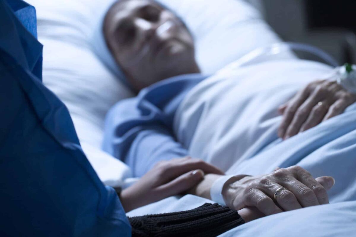 Il "coma irreversibile", cos'è e quanto può durare? - Young woman saying goodbye to her mother dying of cancer in a hospice, holding her hand
