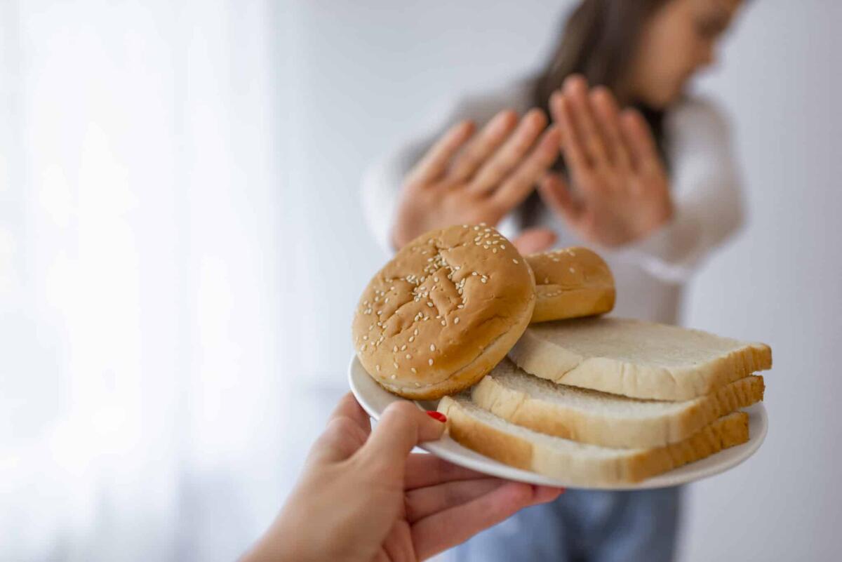 Uno studio ha trovato un metodo per diagnosticare la celiachia con un prelievo di sangue - Young woman suffers from a gluten. Gluten intolerant and Gluten free diet concept, Real people. Copy space. Gluten intolerance and diet concept. Woman refuses to eat white bread. Selective focus on bread