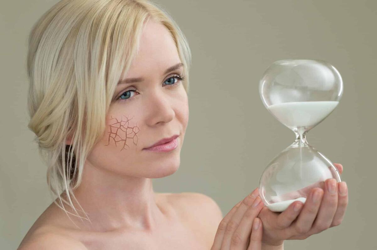 Uno studio conferma: essere ottimisti aiuta a rallentare l'invecchiamento - Beauty portrait of young woman holding hour glass sand timer, aging process concept