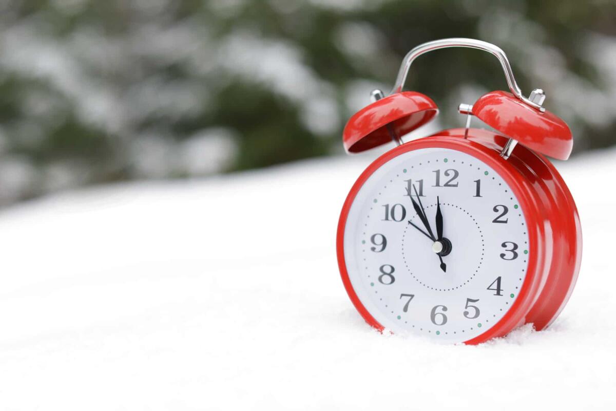Cambio all'ora solare ottobre 2023: dobbiamo spostare l'ora avanti o indietro? - Red alarm clock on white snow outdoors. Space for text