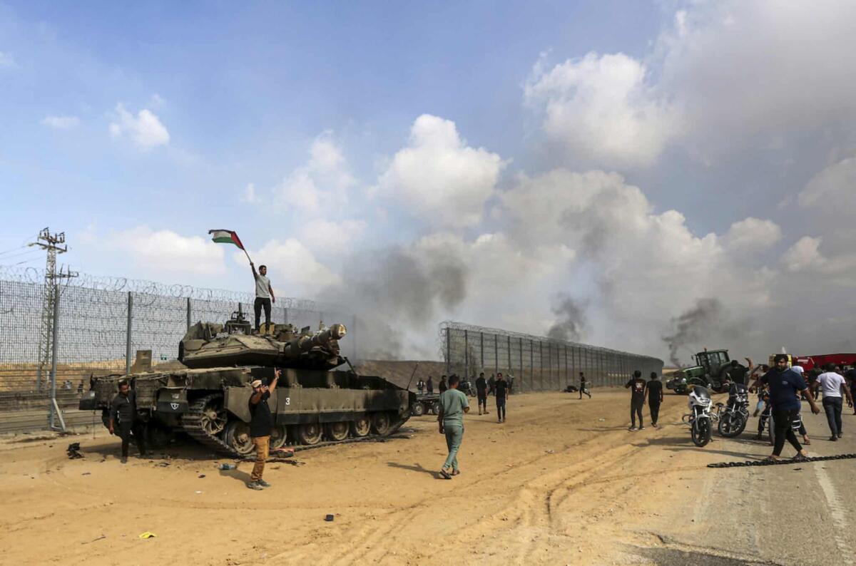 Israele sotto attacco, gli ultimi aggiornamenti - Palestinians wave their national flag and celebrate by a destroyed Israeli tank at the Gaza Strip fence east of Khan Younis southern Saturday, Oct. 7, 2023. The militant Hamas rulers of the Gaza Strip carried out an unprecedented, multi-front attack 