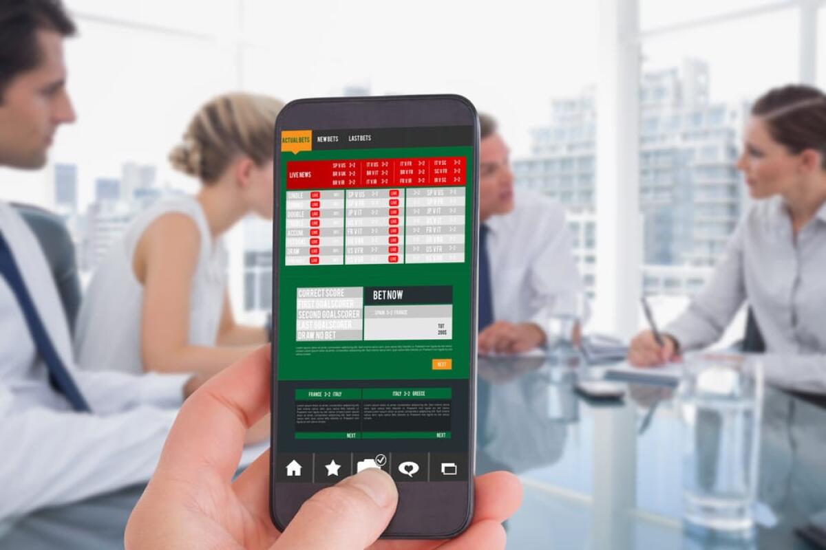 Calcioscommesse: cosa è successo e i calciatori coinvolti - Female hand holding a smartphone against serious businessman during a meeting talking to his employees