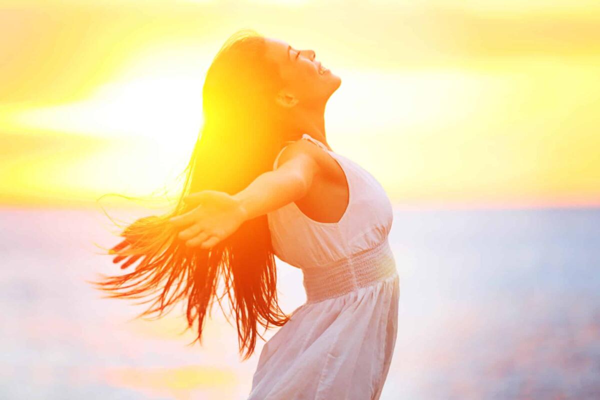 Uno studio conferma che l'esposizione alla luce naturale diminuisce i disturbi mentali - Enjoyment - free happy woman enjoying sunset. Beautiful woman in a white dress embracing the golden sunshine glow of sunset with her arms outspread and face raised to the sky enjoying peace and serenity of nature