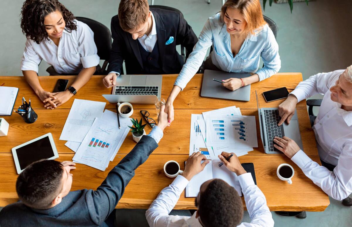 Secondo l'ISTAT il tasso occupazionale di agosto 2023 sale al 61,5% - Business Partners Shaking Hands During Corporate Meeting Sitting At One Table In Modern Office. Above View, Selective Focus