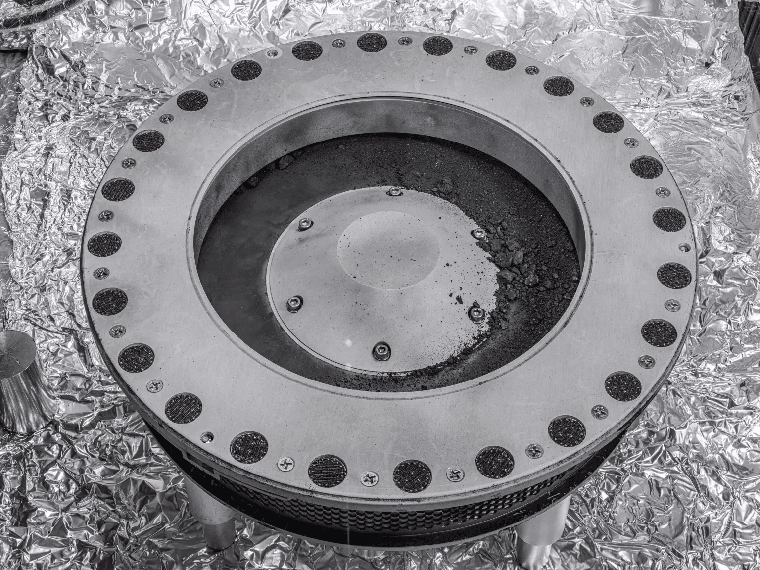 Una vista dell'esterno del raccoglitore di campioni OSIRIS-REx.  Il materiale campione dell'asteroide Bennu può essere visto in centro a destra. Gli scienziati hanno trovato prove sia di carbonio che di acqua nell'analisi iniziale di questo materiale. La 