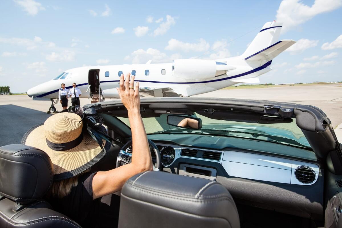 Secondo un rapporto di Oxfam, l'1% più ricco inquina quanto 5 miliardi di persone - Woman in convertible waving hand to pilot and stewardess against private jet at airport terminal
