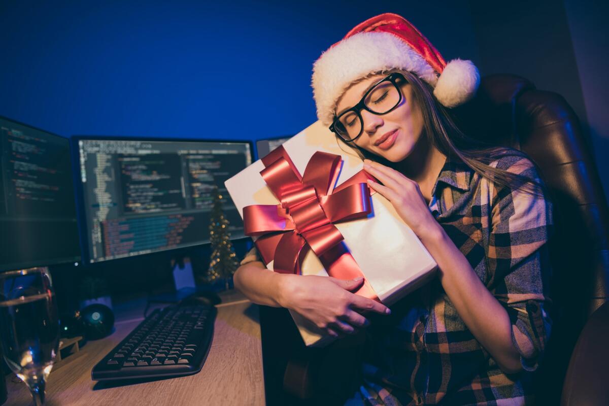 Regalo di Natale per un ingegnere? Approfitta delle offerte del Black Friday - Photo of programmer lady work late night meet newyear alone office workaholic, hugging big giftbox appreciate colleagues corporate surprise wear santa cap glasses indoors