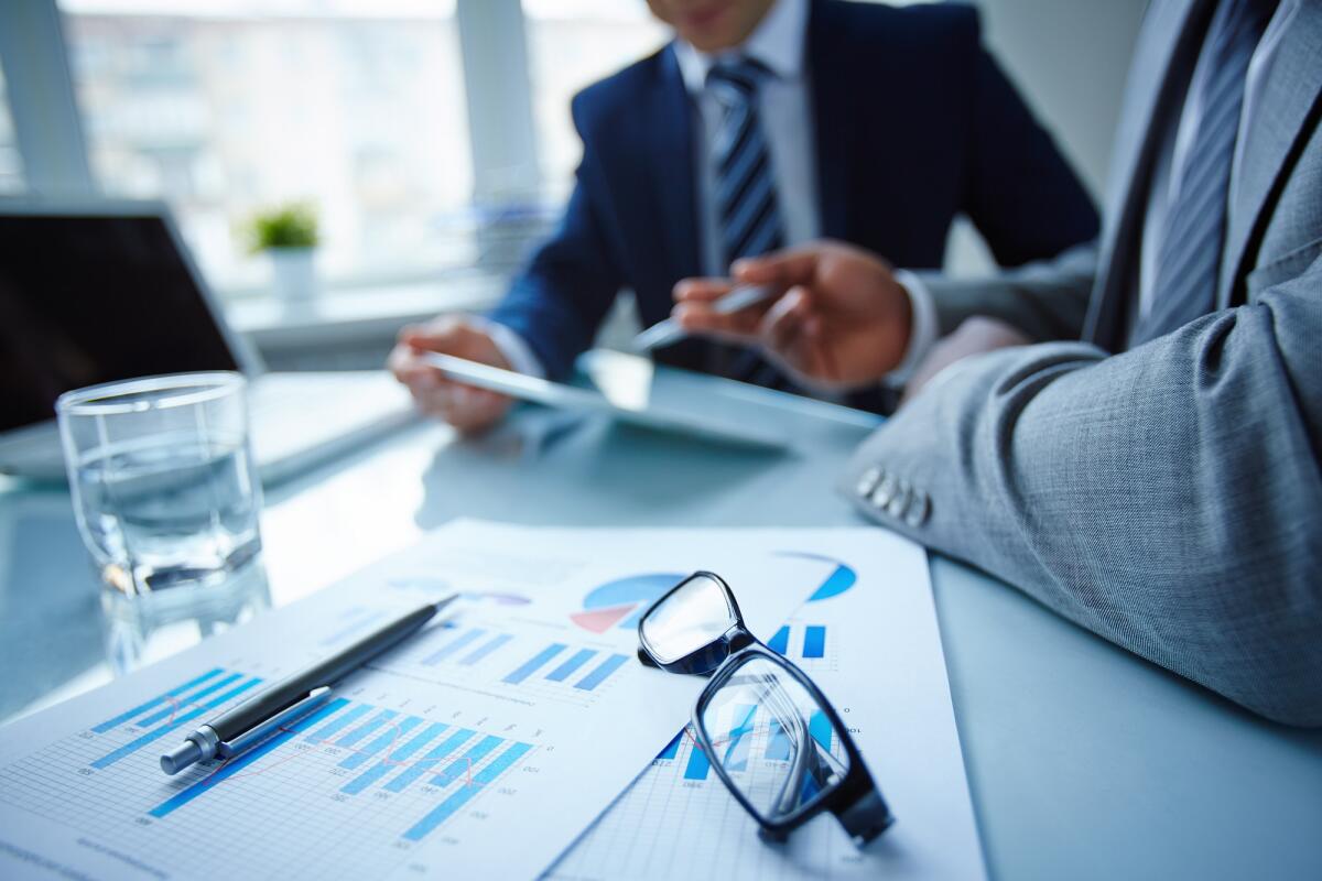 Migliorare la brand reputation: come aprirsi ai confini internazionali del fare business - Image of eyeglasses and financial documents at workplace with businessmen discussing ideas near by