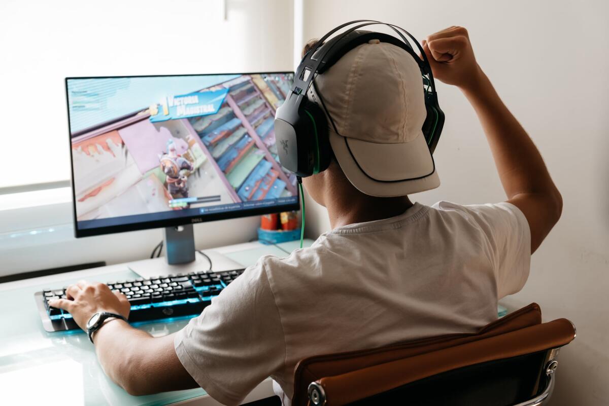 Epic Games vince contro Google e il suo monopolio sulle app Android - Madrid, Spain - August 15, 2018: Teenager playing Fortnite video game on PC. He is raising his fist in a victory gesture. Fortnite is an online multiplayer video game developed by Epic Games