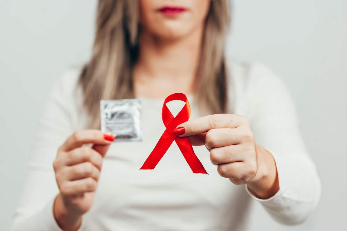 Giornata Mondiale contro l'AIDS: HIV in crescita dopo la pandemia - Woman holding condom and red ribbon for HIV illness awareness, 1 December World AIDS Day concept.