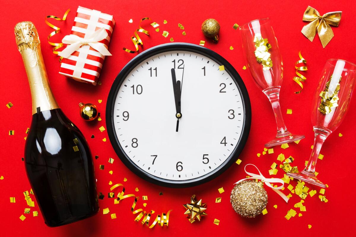 10 cose che (forse) non sapevi sul Capodanno - New year celebration concept with a bottle of champagne and two glasses toasting. Christmas gift box, alarm clock and fir tree branch on colored table. Top view Copy space.