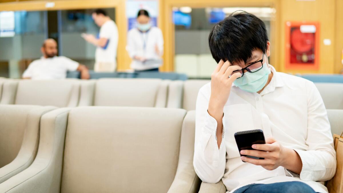 Quattro anni fa veniva scoperto il primo caso di Covid-19 a Wuhan, in Cina - Male Asian patient wearing surgical mask using smartphone at waiting area in hospital or medical center. Medical exam or body check up. Wuhan coronavirus outbreak prevention. Health care concept