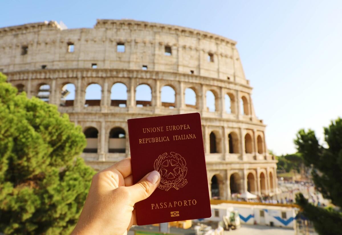Il passaporto italiano è il più forte al mondo nel 2024 (insieme ad altri 5) - Citizenship concept: hand hold Italian passport in front of Colosseum in Rome.